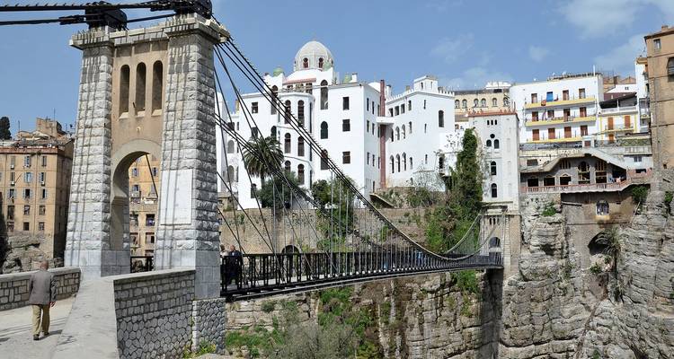 Puente colgante histórico que cruza un profundo desfiladero con edificios blancos de la era otomana de Constantina al fondo.
