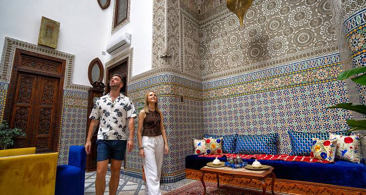 Deux voyageurs admirent les détails complexes de mosaïque et de bois sculpté dans la cour intérieure d'un riad marocain traditionnel.