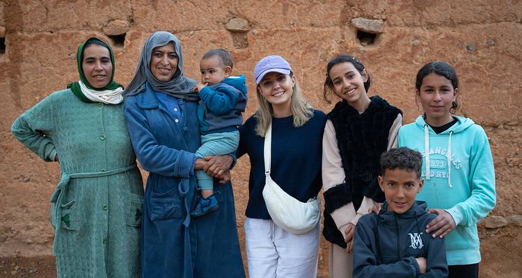 Un touriste pose avec des femmes et des enfants du coin contre un mur en terre dans un village marocain.