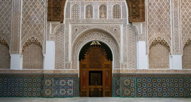 Entrée minutieusement sculptée et carrelée d'une médersa marocaine avec une porte en bois ornée