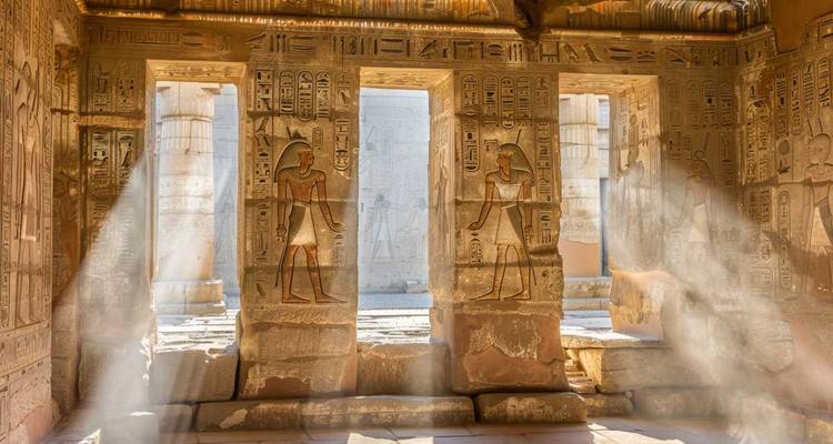 Des rayons de soleil filtrent à travers des colonnes sculptées couvertes d'hiéroglyphes à l'intérieur d'un temple égyptien antique.