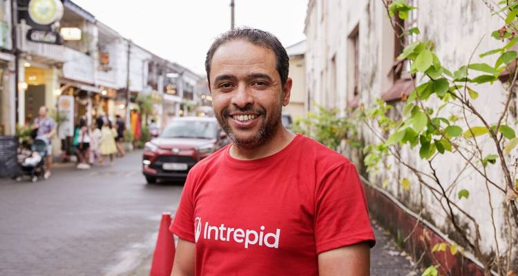 Guide touristique souriant portant un T-shirt rouge Intrepid se tient dans une rue coloniale animée.