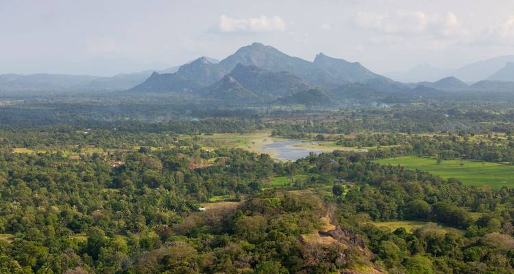 Vue expansive de la vallée avec des crêtes montagneuses lointaines et des champs en patchwork sous une lumière brumeuse.