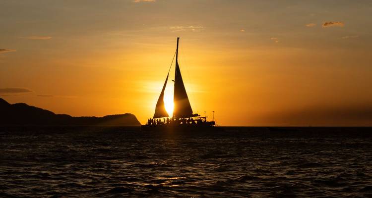 Silhouettiertes Segelboot gleitet bei dramatischem orangefarbenem Sonnenuntergang über den Ozean.