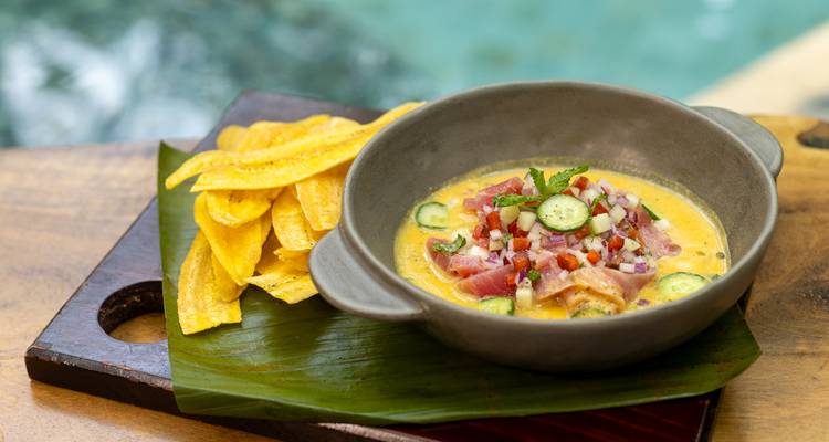 Un bol de ceviche coloré garni de concombre est posé à côté de chips de banane plantain frites au bord d'une piscine.