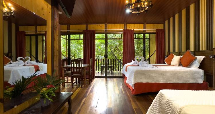 Chambre élégante de lodge dans la jungle avec parquet, accents rouges et grandes fenêtres ouvrant sur une végétation luxuriante.