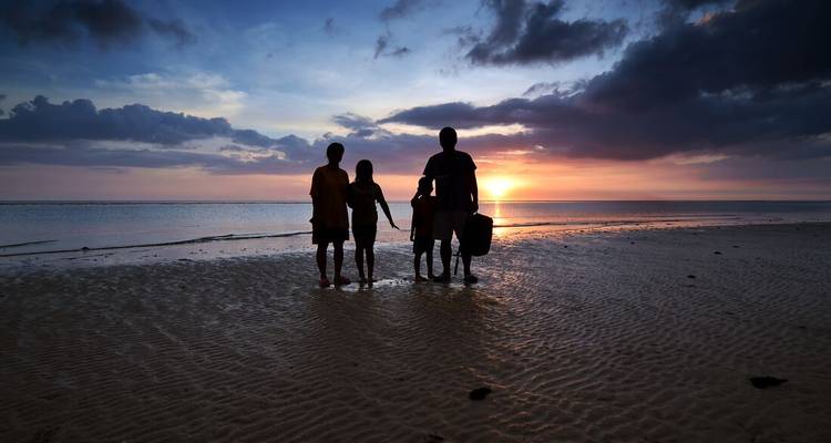 Une famille en silhouette se tenant la main regarde un coucher de soleil dramatique sur une plage calme.