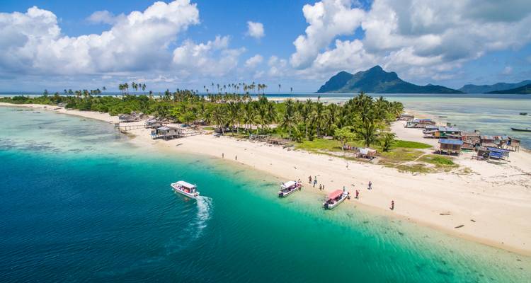 Vue aérienne d'une plage d'île tropicale avec une eau turquoise et de petits bateaux ancrés près du rivage.
