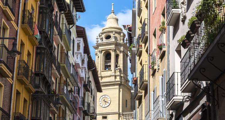 Une tour d'horloge en pierre s'élève entre d'étroits balcons colorés dans la vieille ville de Pampelune.