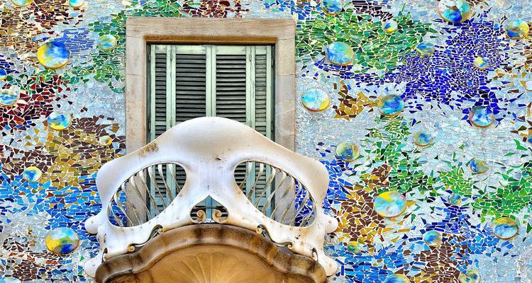 Gros plan vibrant de la façade en mosaïque colorée de Gaudí et du balcon ossiforme de la Casa Batlló avec fenêtre à volets.