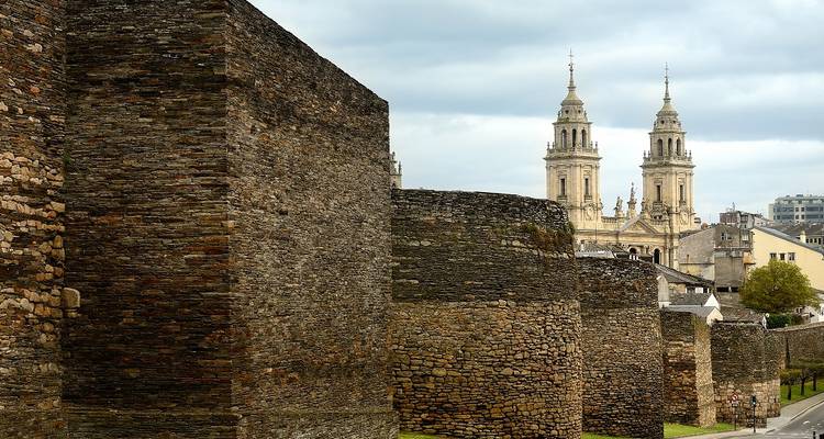 Massifs murs romains en pierre de Lugo menant à une cathédrale aux tours jumelles sous un ciel nuageux.