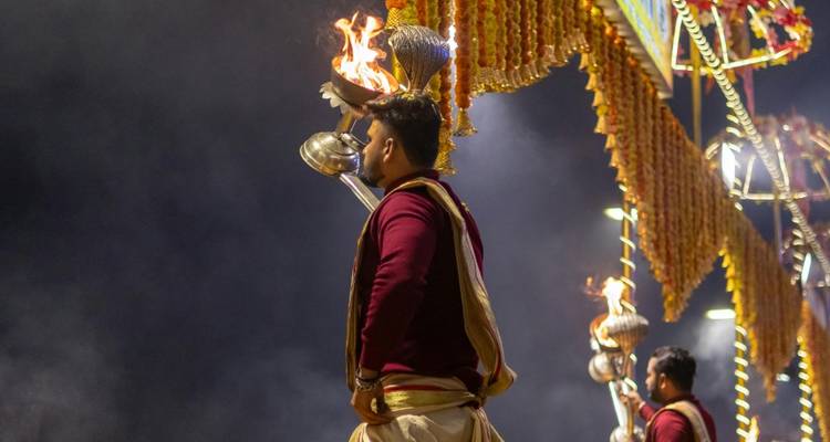 Priesters voeren een avond Ganga Aarti uit, waarbij ze brandende koperen lampen vasthouden tegen een rokerige nachtelijke hemel.