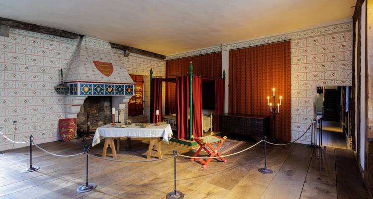 Chambre de château médiéval avec lit à baldaquin, cheminée peinte et barrières de corde sur plancher de bois