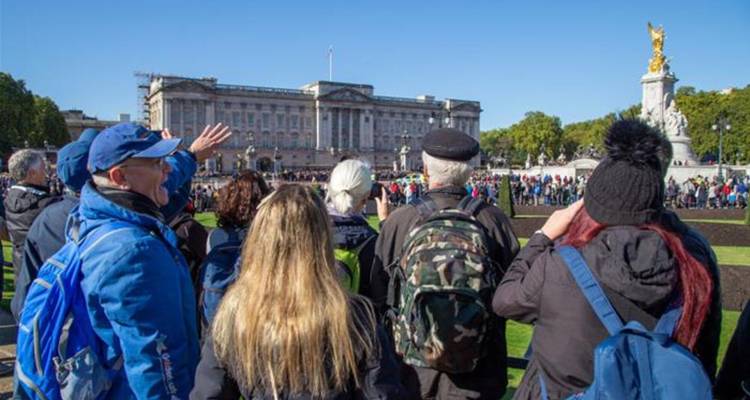 Des touristes rassemblés sur une pelouse face au palais de Buckingham, certains pointant des appareils photo par une journée ensoleillée