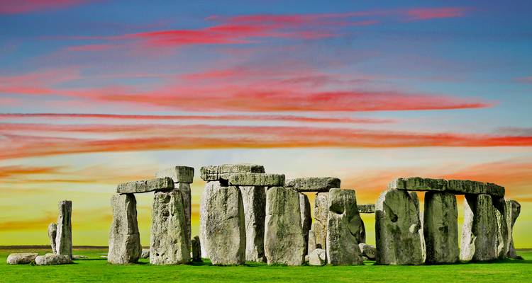 Stonehenge en silhouette contre un ciel de coucher de soleil aux couleurs vives et multicolores au-dessus d'une herbe verte luxuriante