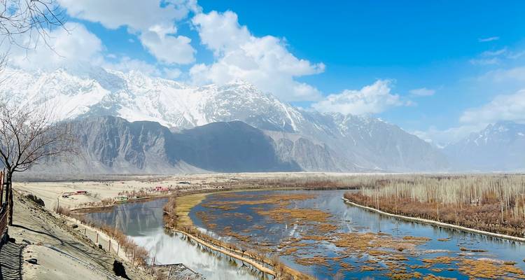 Wide river meandering through a barren valley beneath towering snow-covered mountains.