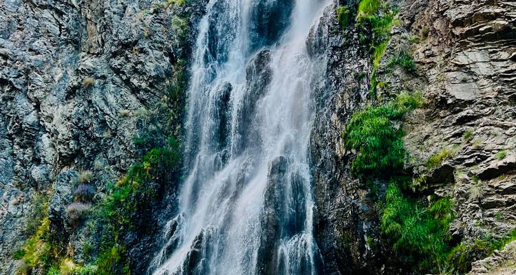 Powerful waterfall cascading down rugged rock cliffs surrounded by greenery.