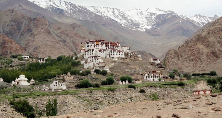 A hillside monastery complex nestles beneath rugged, snow-streaked mountains in Ladakh.