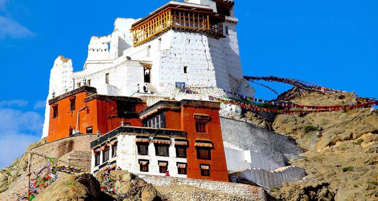 A white hilltop fortress festooned with prayer flags stands against a brilliant blue sky.