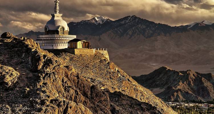 The white dome of Shanti Stupa crowns a rocky ridge at sunset with shadowed peaks beyond.