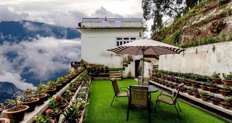 A rooftop garden with potted plants and patio furniture floats above mist-filled mountain valleys.
