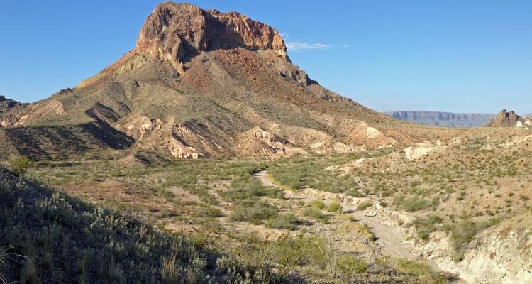 Une mesa rocheuse aride s'élève au-dessus d'une vallée désertique sous un ciel sans nuages.