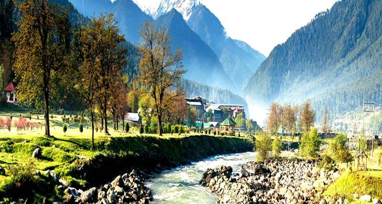 Vista panorámica clara de un río de corriente rápida con orilla pedregosa, prados verdes, casas dispersas y altas montañas nevadas detrás bajo la luz solar brillante