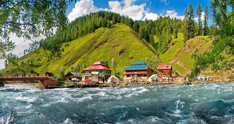 Rivière de montagne tumultueuse avec des chalets en bois colorés au pied de collines verdoyantes et de forêt