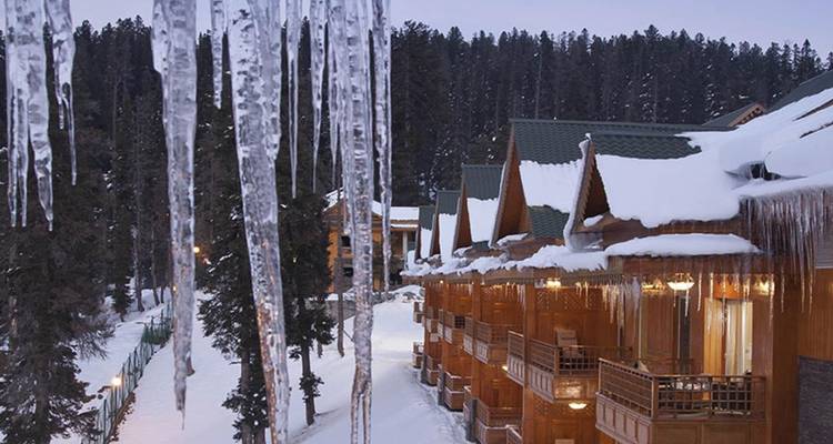 Des stalactites de glace pendent du toit des balcons d'un chalet en bois surplombant une forêt enneigée au crépuscule
