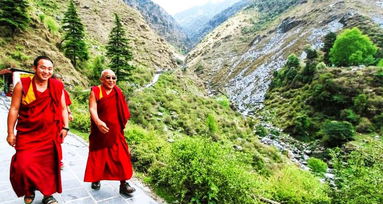 Two smiling monks in red robes walking along a mountain path with a deep valley behind.