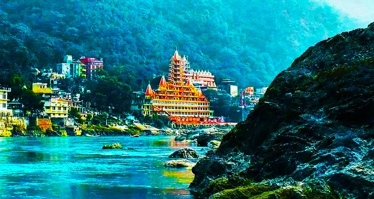 Colourful temple complex on the banks of the Ganges surrounded by steep green hills in Rishikesh.