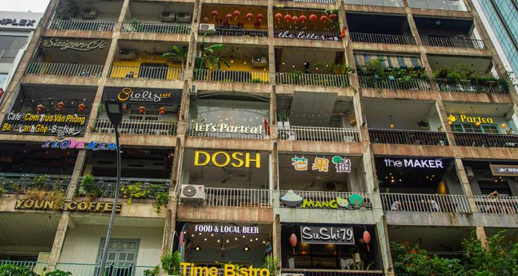 Appartementenblok van meerdere verdiepingen gevuld met kleurrijke café-uithangborden en balkons in een stedelijke omgeving.