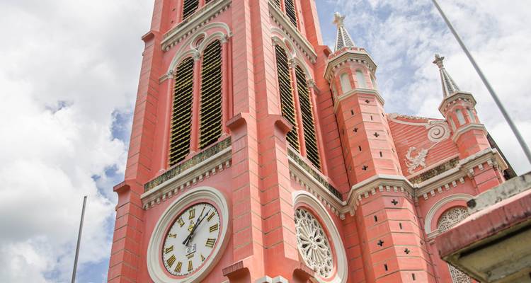 Dichtbij zicht van de roze klokkentoren van de Tan Dinh Kerk met sierlijke details tegen een gedeeltelijk bewolkte hemel.