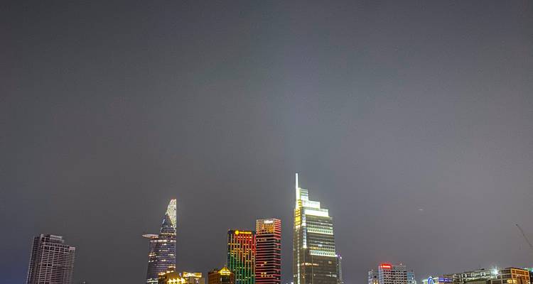 Nachtelijke skyline van Ho Chi Minh-stad met verlichte wolkenkrabbers tegen een donkergrijze hemel.