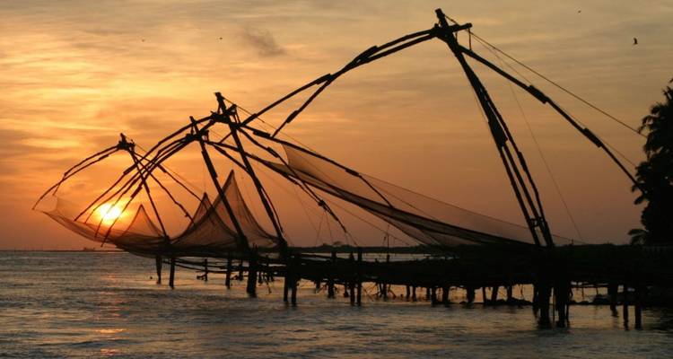 Des filets de pêche chinois se découpent en silhouette contre un coucher de soleil orange alors qu'ils plongent dans la mer d'Arabie à Kochi.