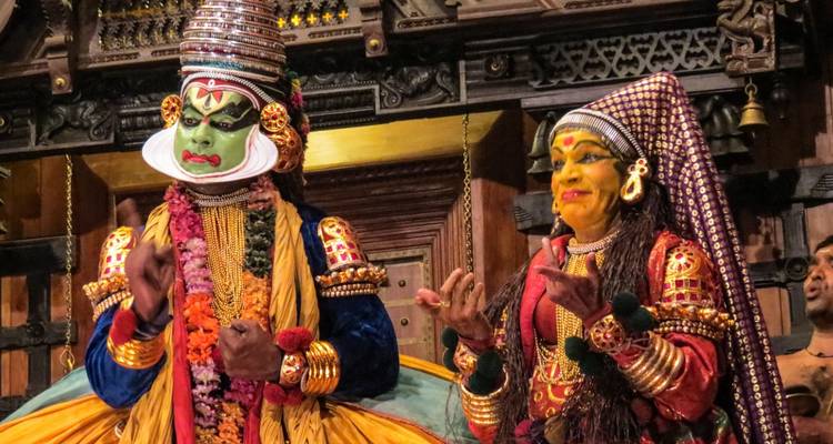 Des interprètes de Kathakali en maquillage coloré élaboré et costumes font des gestes dramatiques sur scène.