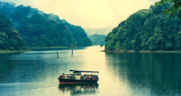 Un petit bateau d'excursion dérive sur les eaux vertes brumeuses du lac Periyar, entouré d'une forêt tropicale dense.