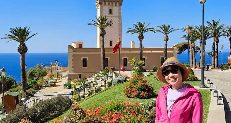 Viajero sonriente se encuentra frente a un faro costero, jardines y palmeras con vista al Océano Atlántico.