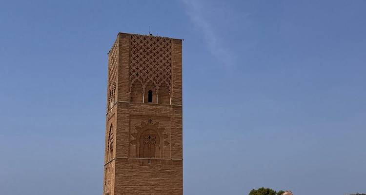 Alto minarete de piedra roja con intrincadas tallas geométricas que se alza contra un cielo azul despejado