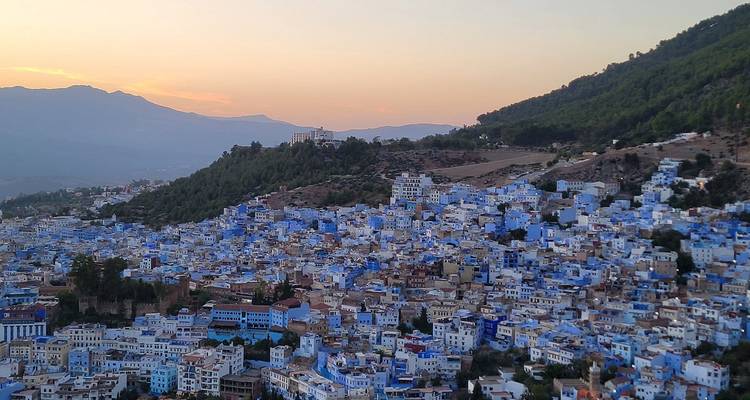 Panoramablick auf Chefchaouens blaue Häuser, die sich bei Sonnenuntergang über die Hügelhänge erstrecken