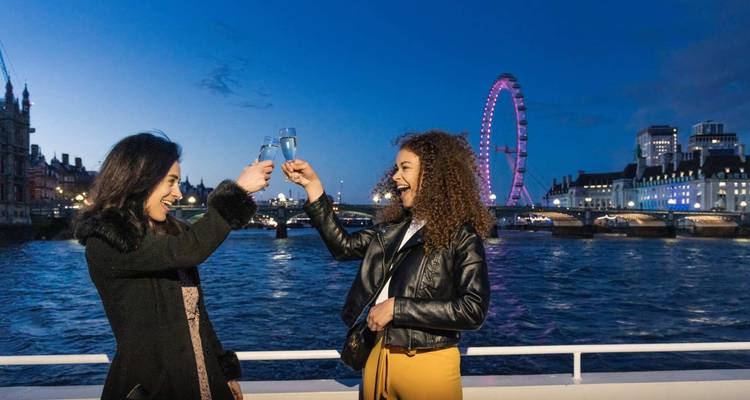 Deux amis portent un toast lors d'une croisière fluviale avec le London Eye illuminé qui se dresse derrière eux au crépuscule.