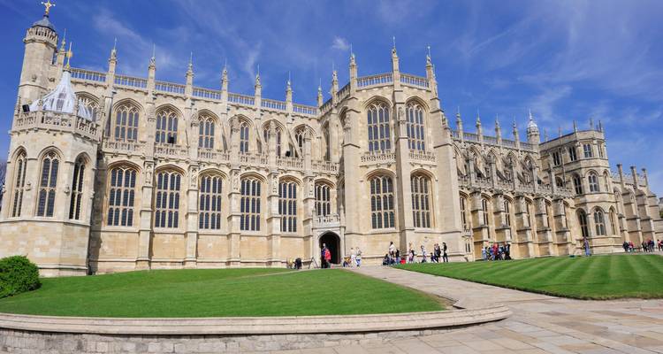 La chapelle gothique Saint-Georges du château de Windsor encadrée par des pelouses luxuriantes et un ciel bleu.