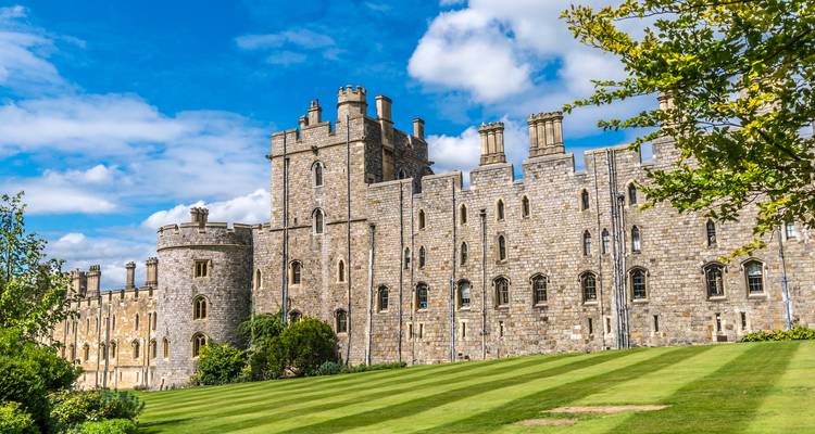 Façade latérale du château de Windsor s'élevant au-dessus de pelouses vertes rayées par une journée ensoleillée et lumineuse avec des nuages épars.