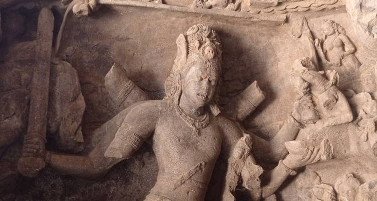 Detailliertes Steinrelief einer vielarmigen hinduistischen Gottheit in einem antiken Höhlentempel.