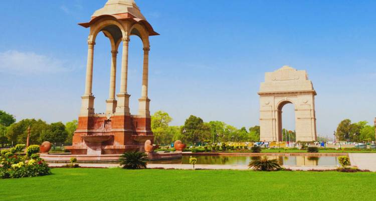 Üppiger grüner Rasen, der zum India Gate und seinem nahegelegenen Baldachin-Monument unter einem hellen Himmel führt.