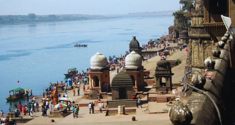 Menschenmengen versammeln sich entlang der breiten Stufen der Maheshwar-Ghats neben dem weiten Narmada-Fluss.