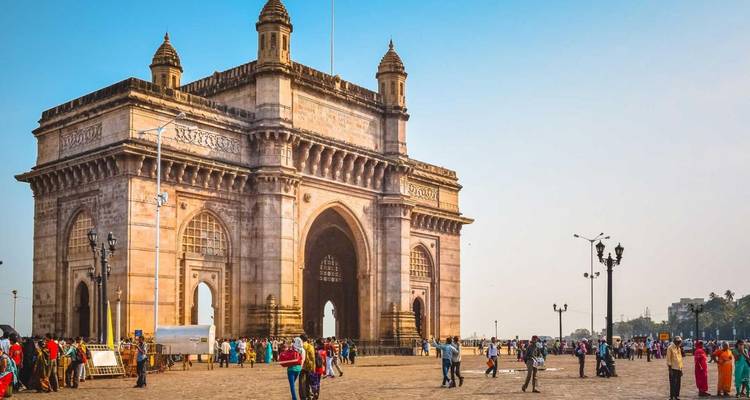 Das Gateway of India Monument erhebt sich über einen belebten Hafenplatz in Mumbai unter einem klaren Morgenhimmel.