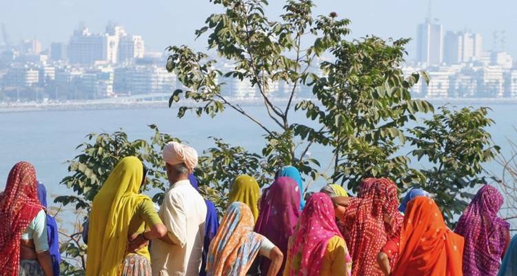 Bunt gekleidete Dorfbewohner in leuchtenden Saris blicken über das Wasser auf Mumbais Skyline.