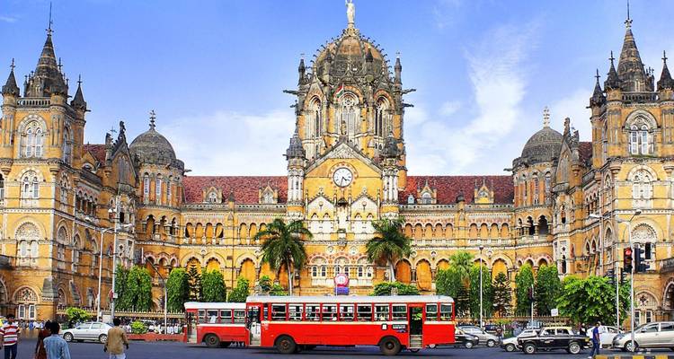 Viktorianisch-gotische Fassade des Chhatrapati Shivaji Terminus mit einem roten Stadtbus, der davor vorbeifährt.