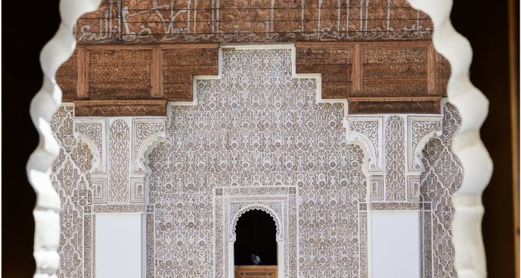 Kunstvolle Stuckarbeiten und Zedernholzgitter einer marokkanischen Madrasa, gerahmt von einem Schlüssellochbogen.